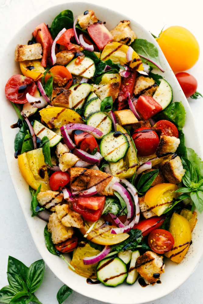 A Panzanella Salad in a white dish with mint leaves around it and tomatoes. 