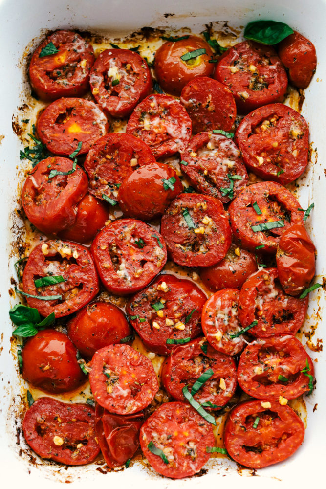 Roasted tomatoes sliced in a pan topped with basil and cheese