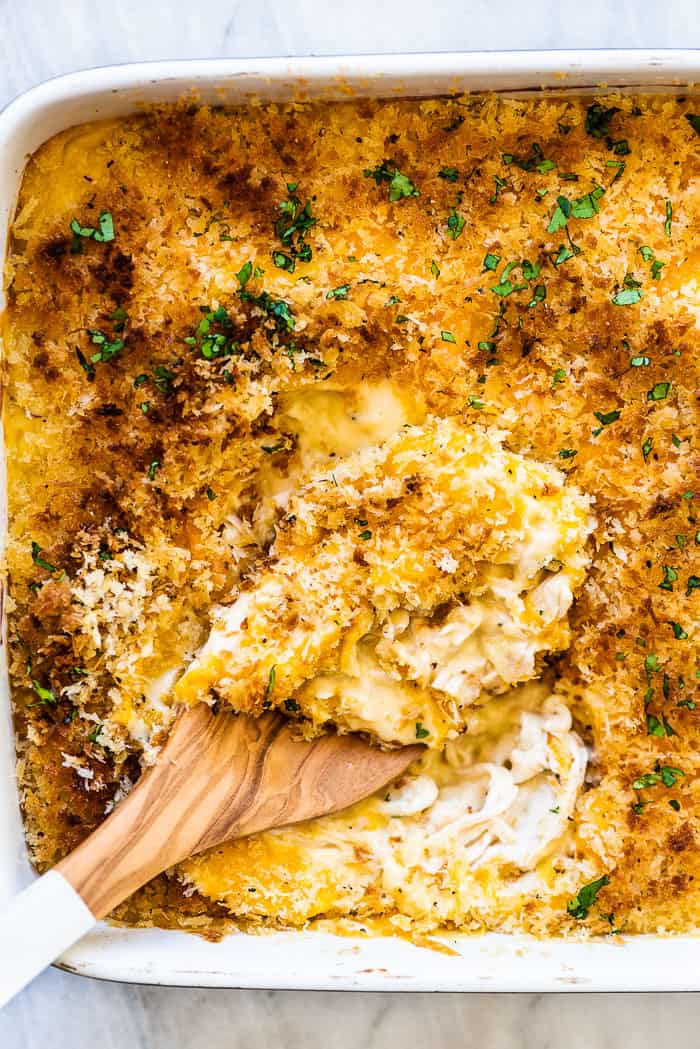 A wooden spoon scooping chicken divan out of a casserole dish.