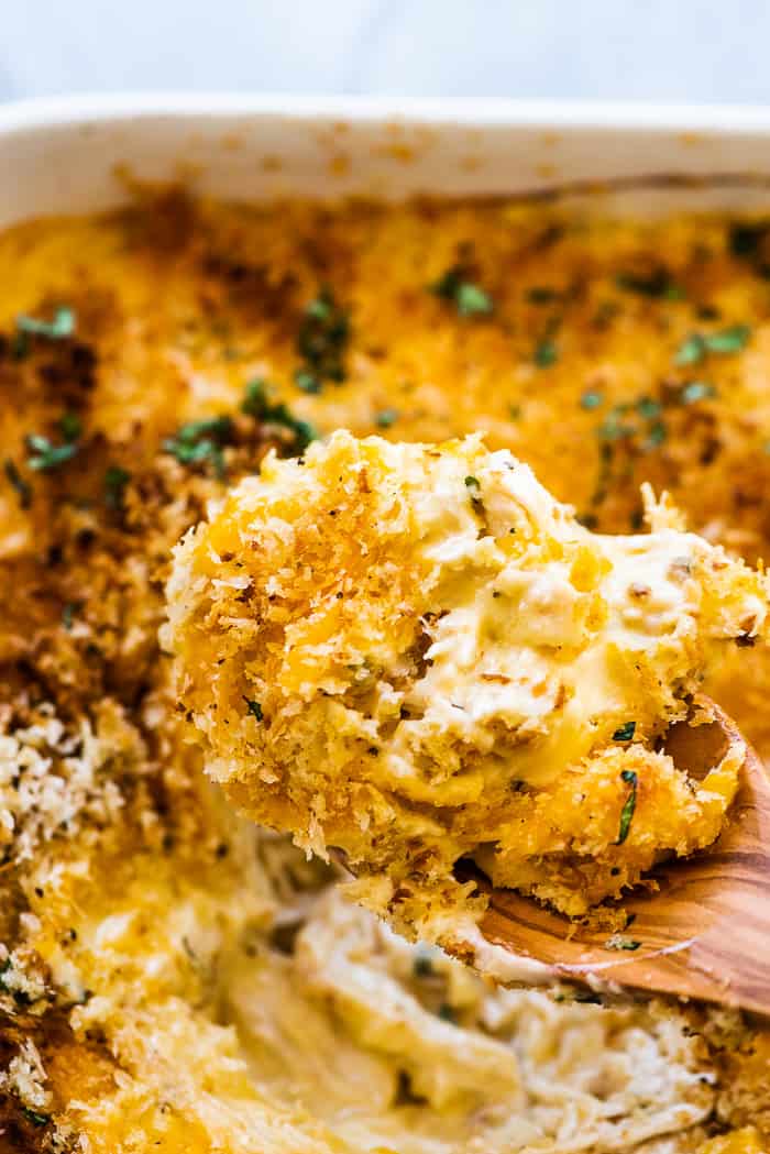 A wooden spoon scooping chicken divan out of a casserole dish.