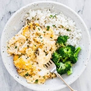 A white bowl with chicken divan with broccoli and rice on the side.