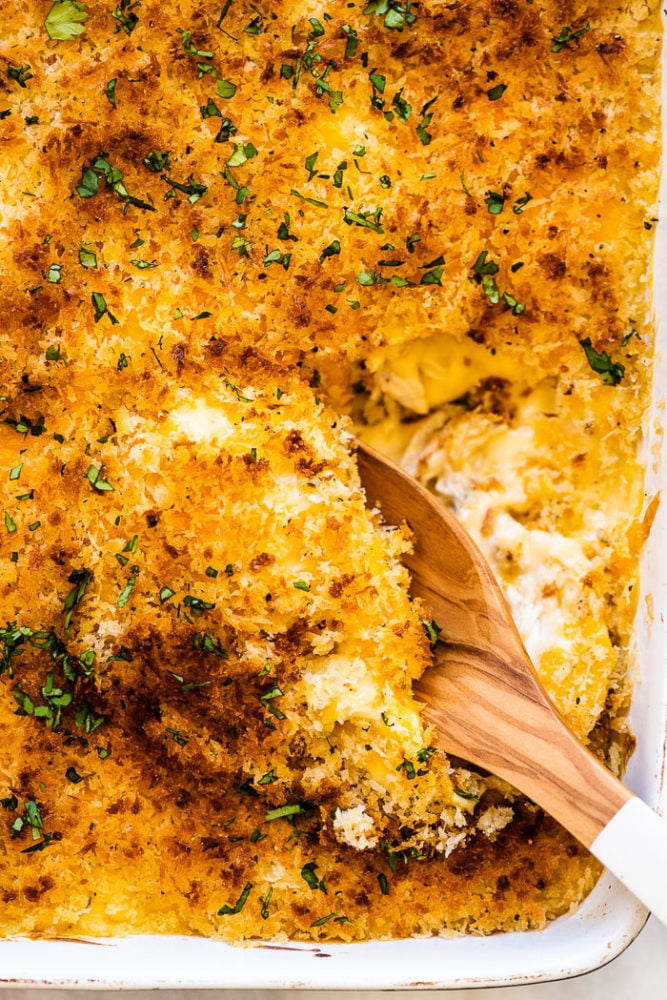 A spoon taking a scoop of chicken divan out of a white casserole dish.