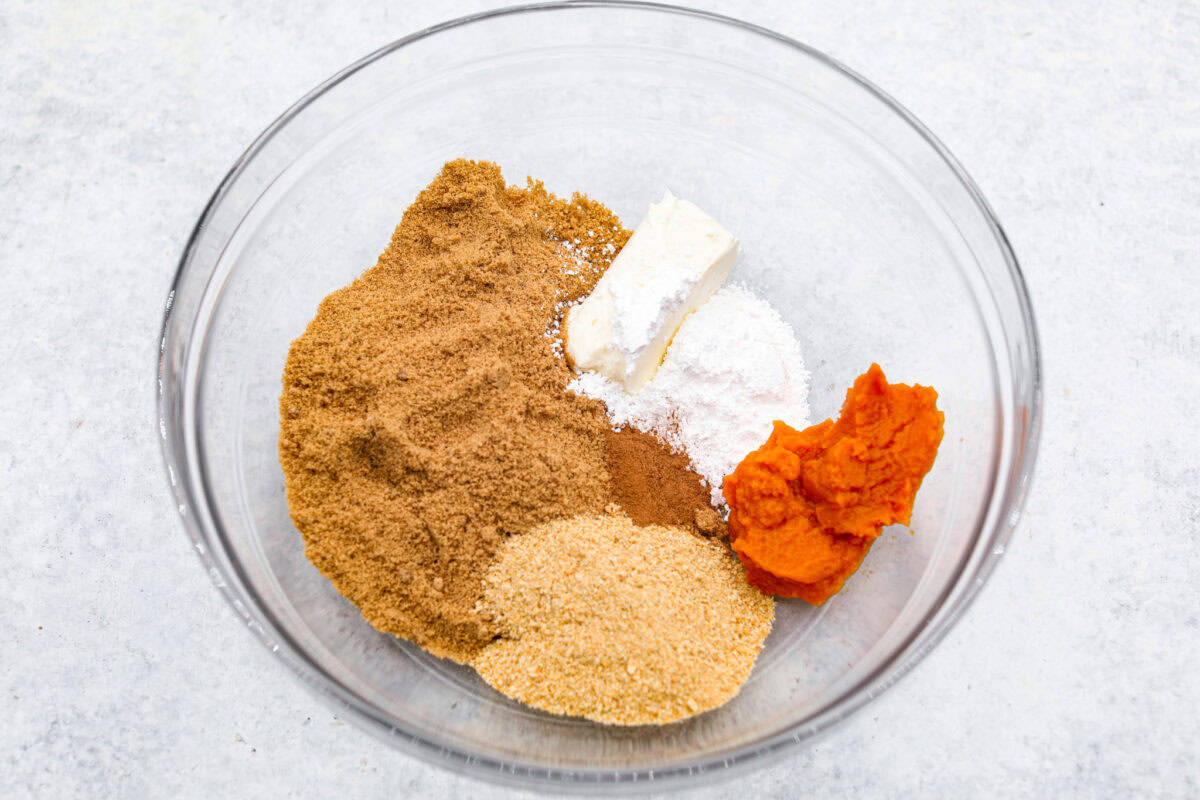 Overhead shot of pumpkin, sugar, cream cheese, graham cracker and gingersnap crumbs in a bowl. 