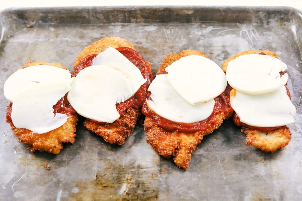 Fried chicken parmesan with marinara and cheese on a sheet pan. 