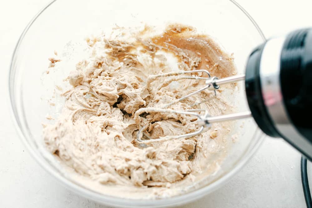 Cinnamon honey butter mixed together in a clear glass bowl with a mixer. 