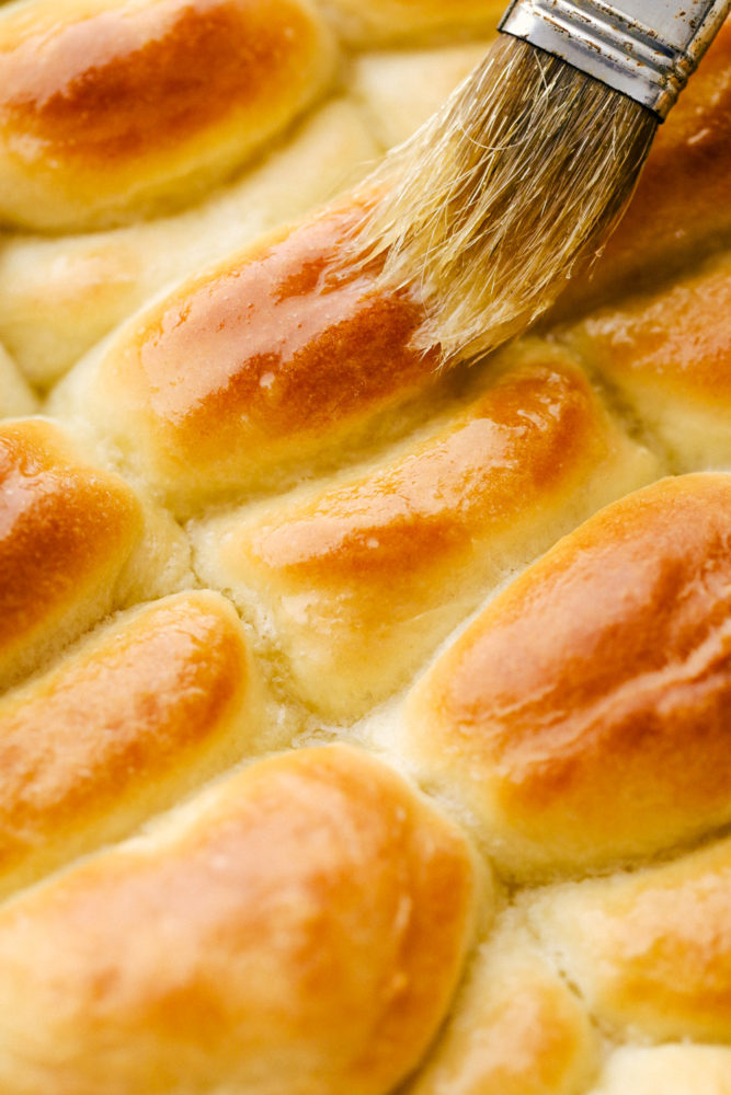 Brushing butter on golden baked Parker House Rolls