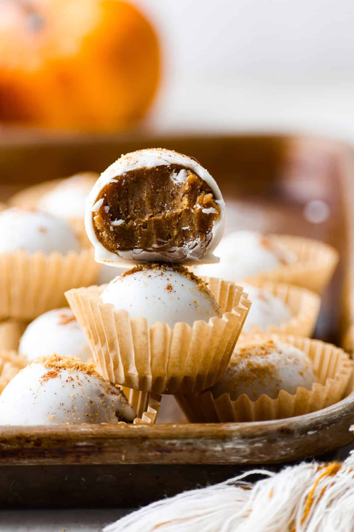 Close up shot of a pumpkin cream cheese truffle stacked on another truffle with a bite taken out of it. 