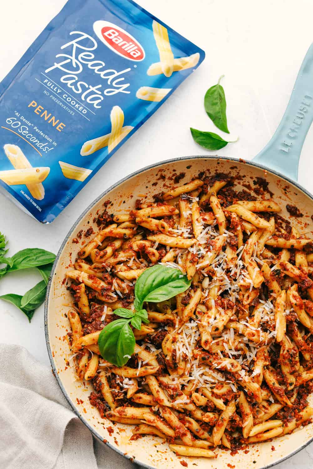 Sun dried tomato pesto pasta in a skillet with a package of ready pasta. 