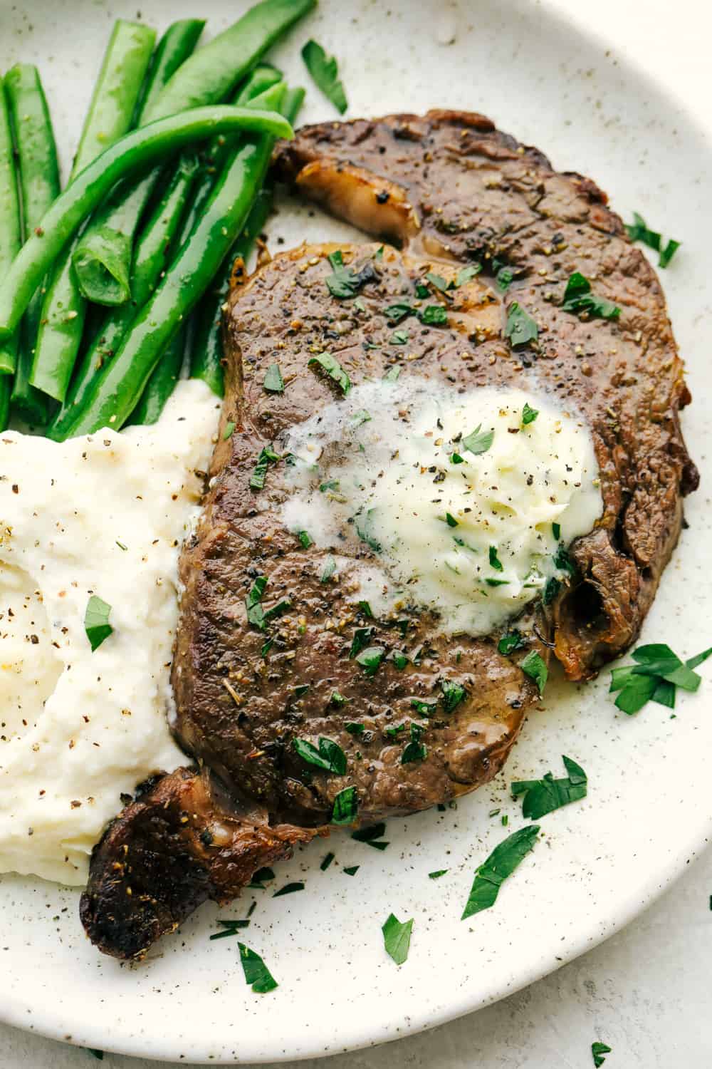 Perfect Air Fryer Steak with golden seared outside and tender juicy inside. Topped with garlic butter and a side of beans and potatoes.