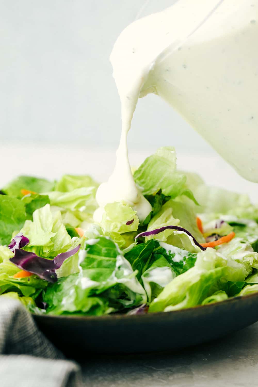 Pouring rich, creamy zesty Homemade Ranch Dressing on Salad.