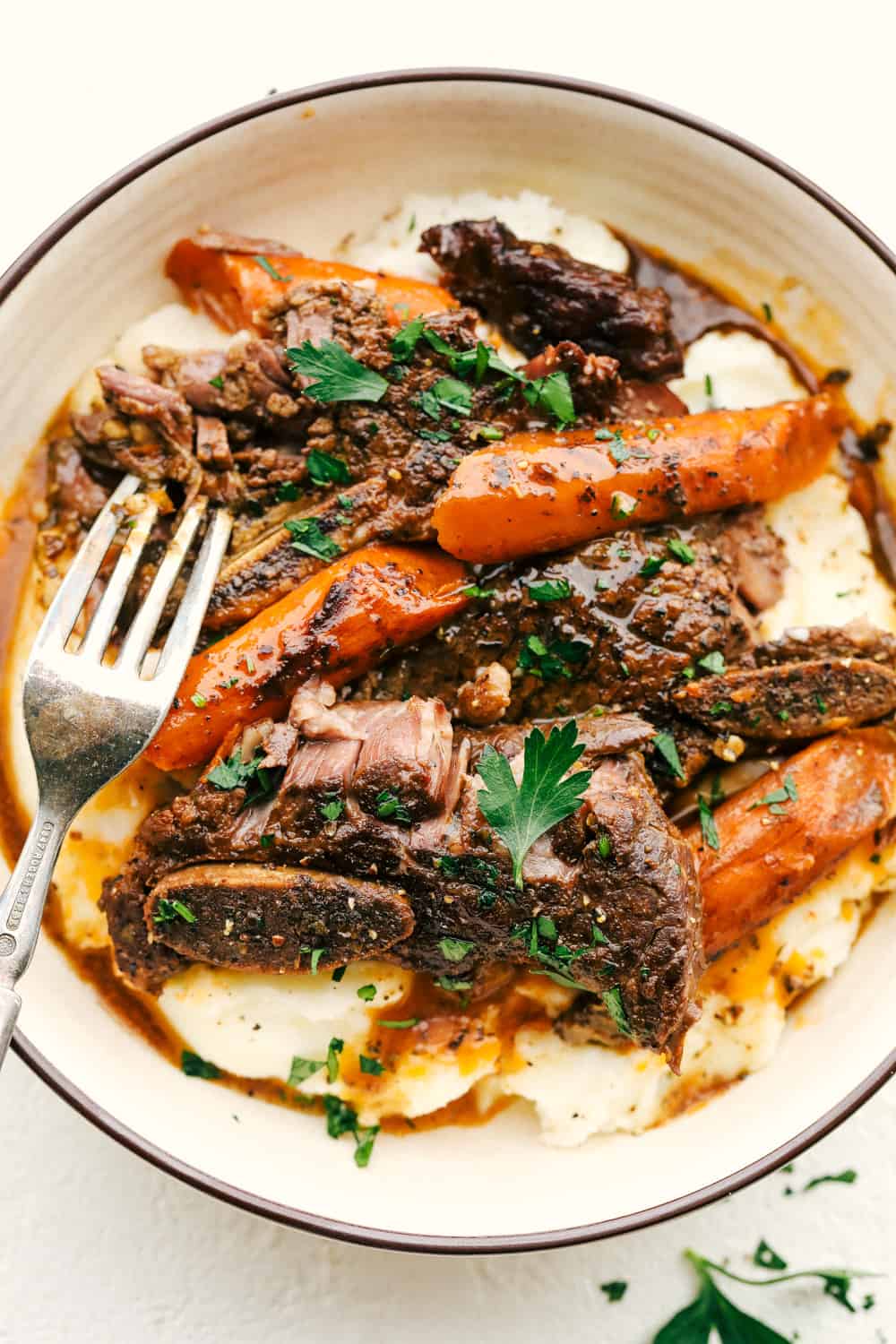 Fork Tender Slow Cooker Short Ribs in a bowl with mashed potatoes and carrots. 