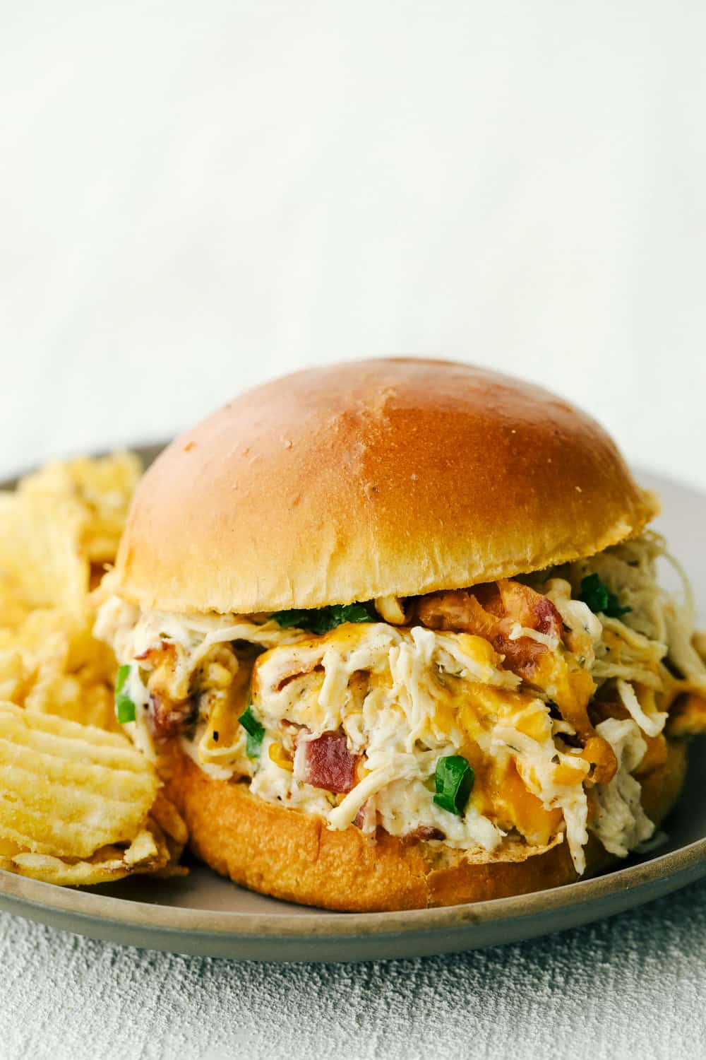 Slow cooker ranch chicken served on a bun alongside potato chips.