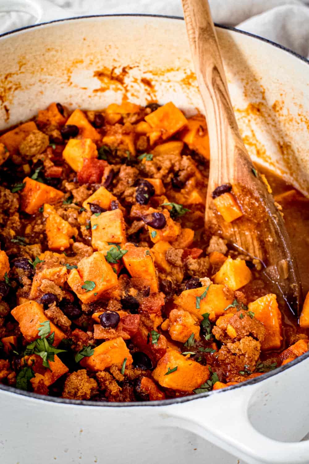 Dutch oven with sweet potato chili and wooden spoon.