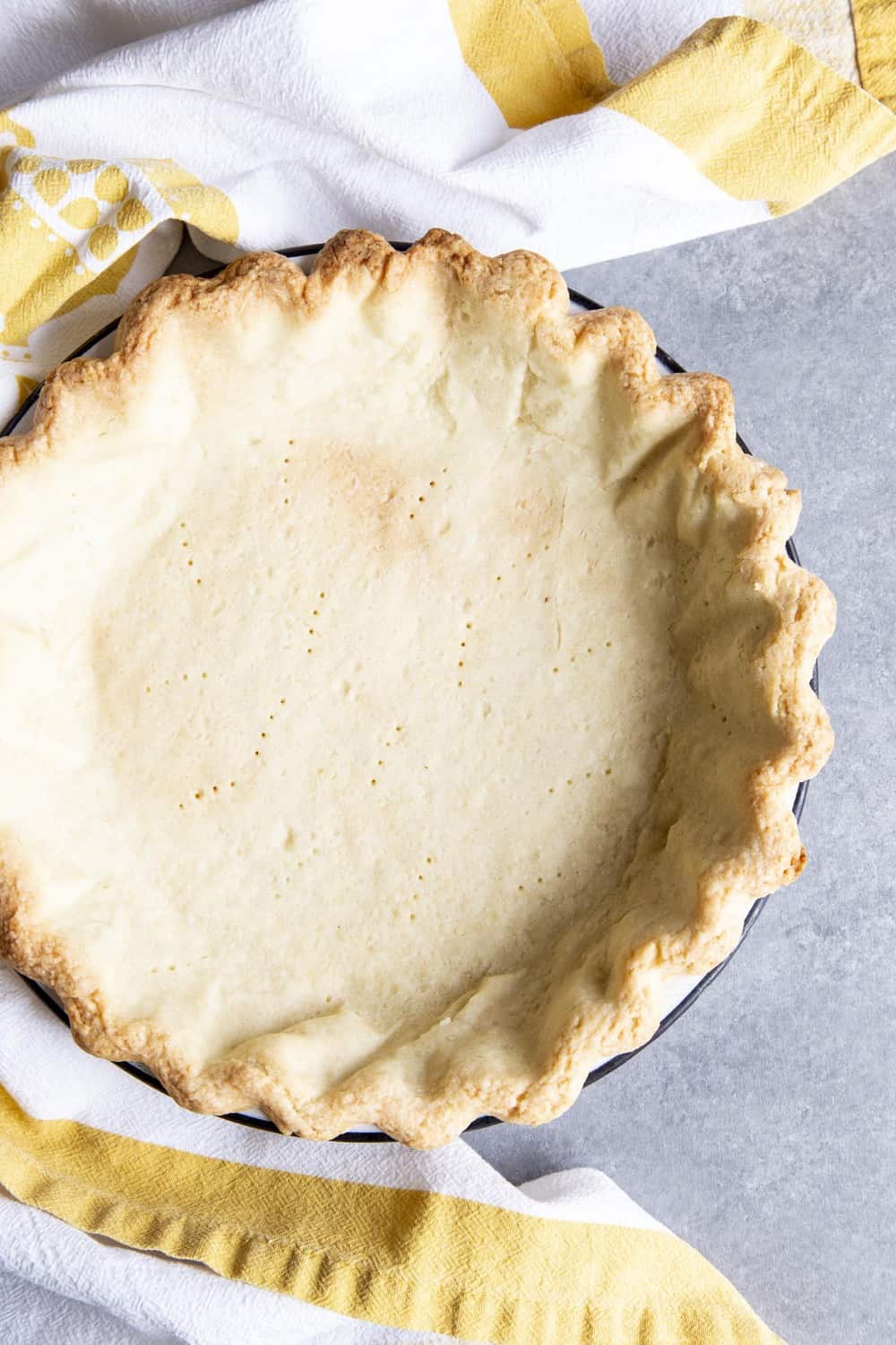 A par-bake pie crust on a gray surface next to a tea towel