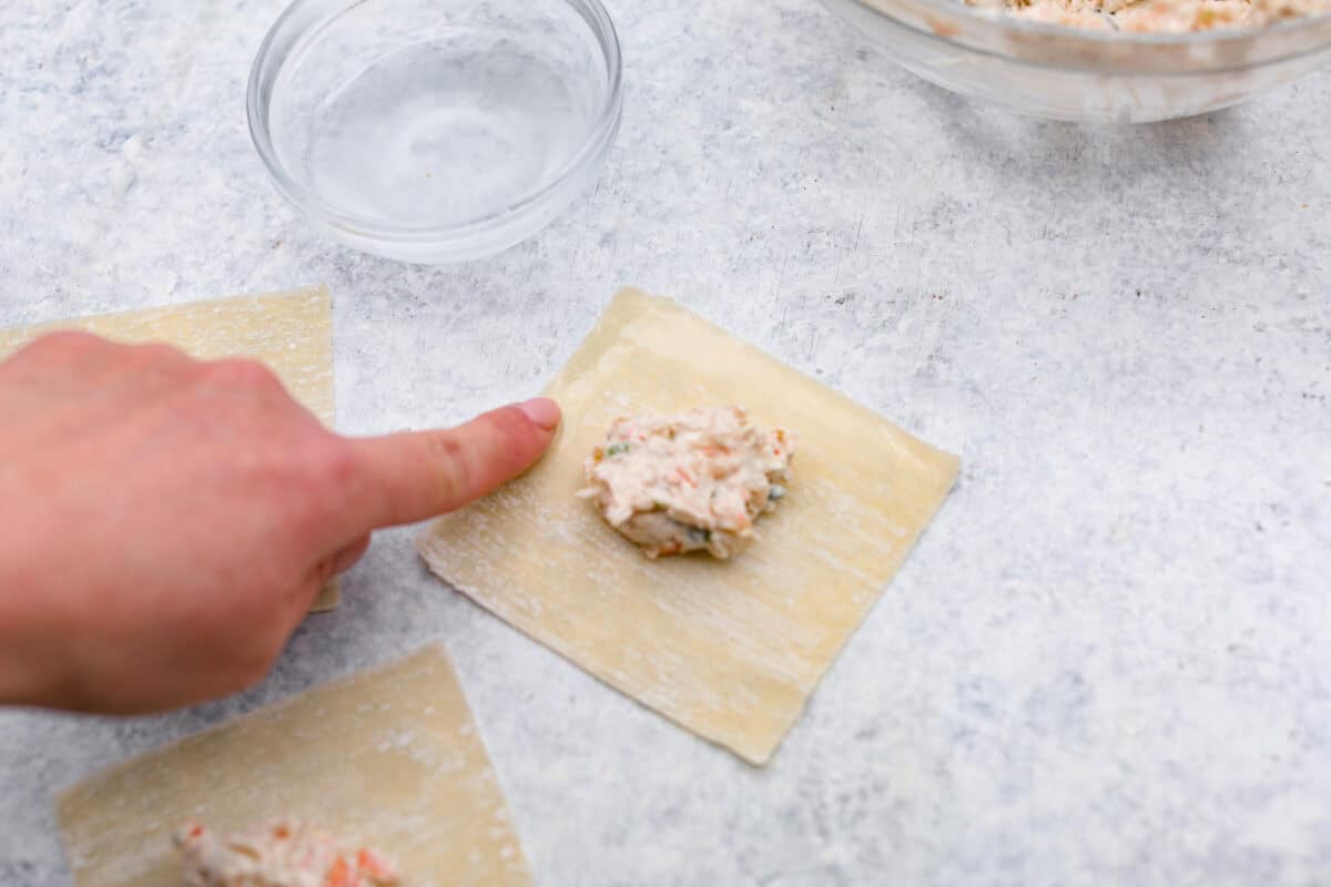 Overhead shot of someone using their finger to wet the edges of the wonton paper. 