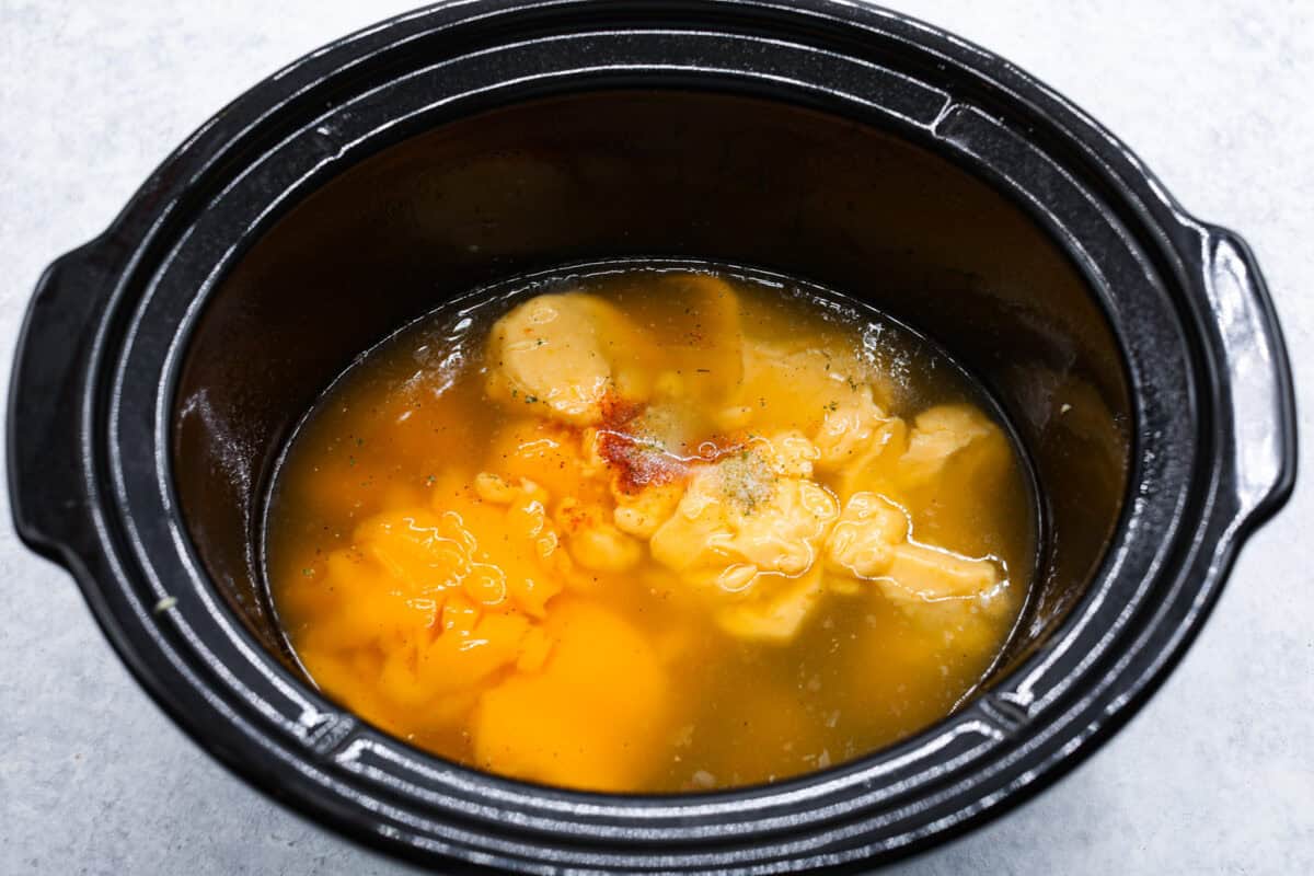 Overhead shot of soups, broth and seasonings in the bottom of a crockpot.