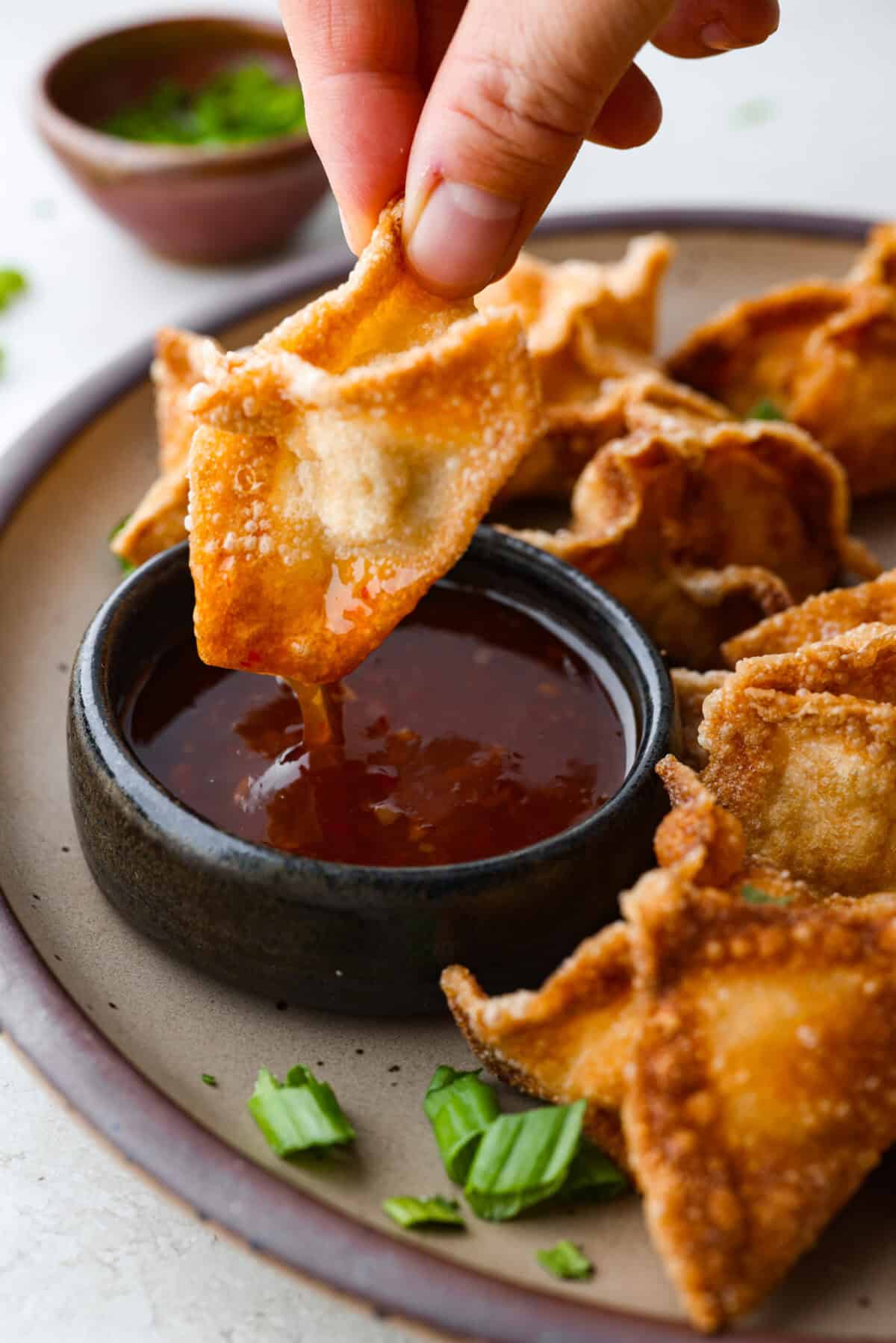 Close up shot of someone dipping their crab rangoon into sauce. 