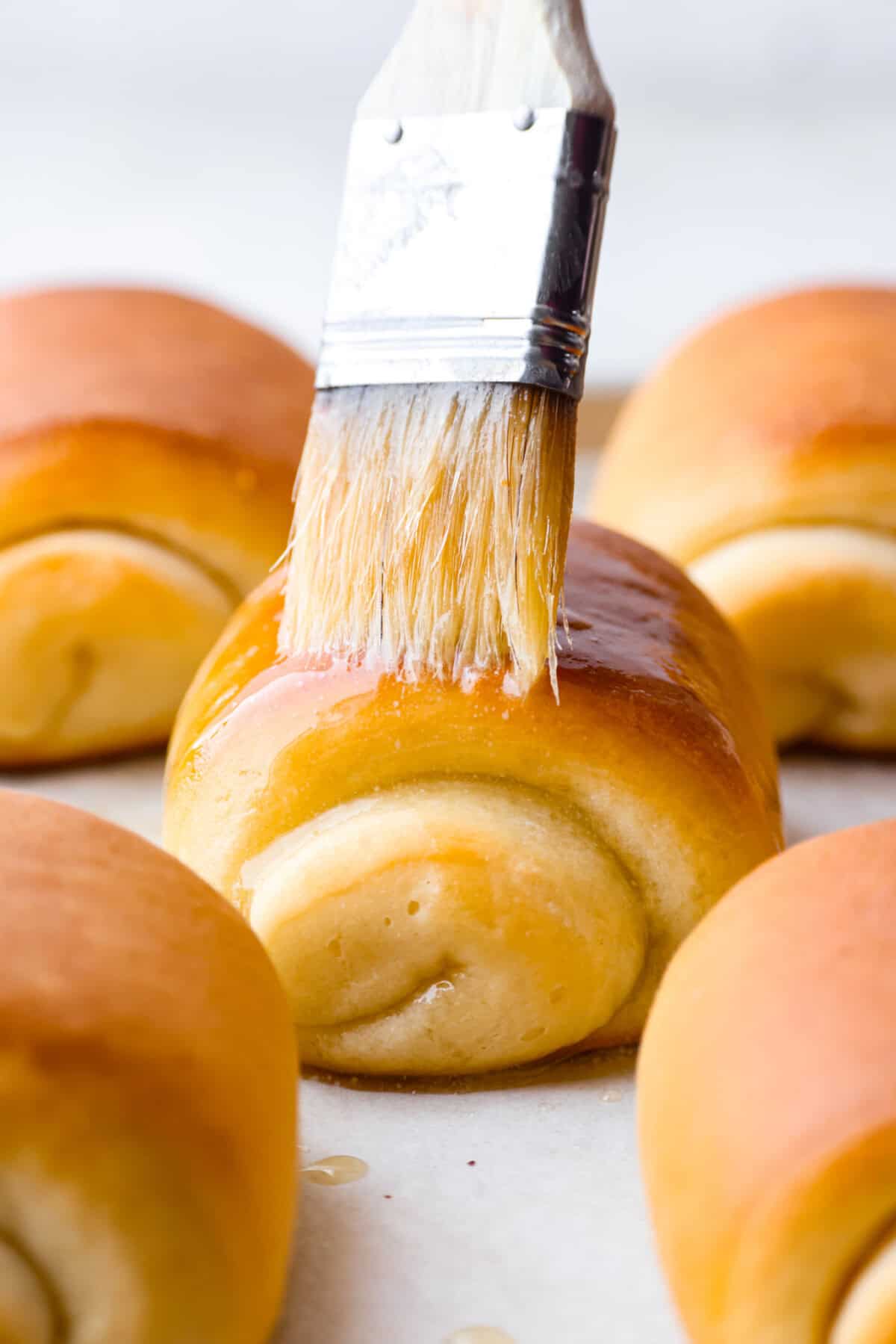 Close up shot of someone spreading butter on top of a lion house roll. 