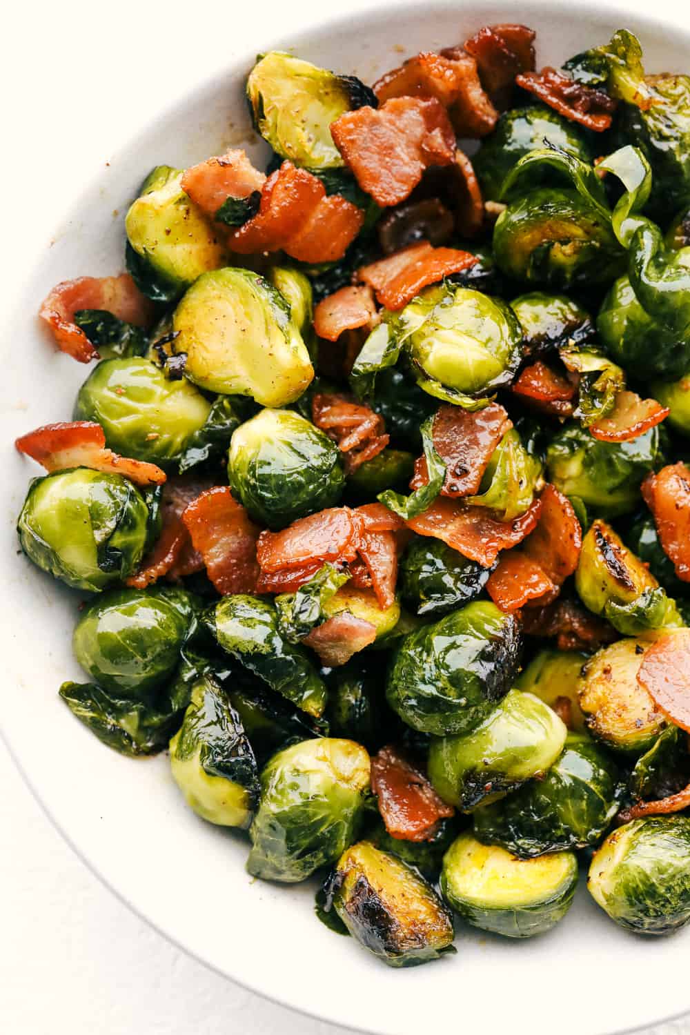 Bacon, brussel sprouts tossed with maple syrup on a white plate.