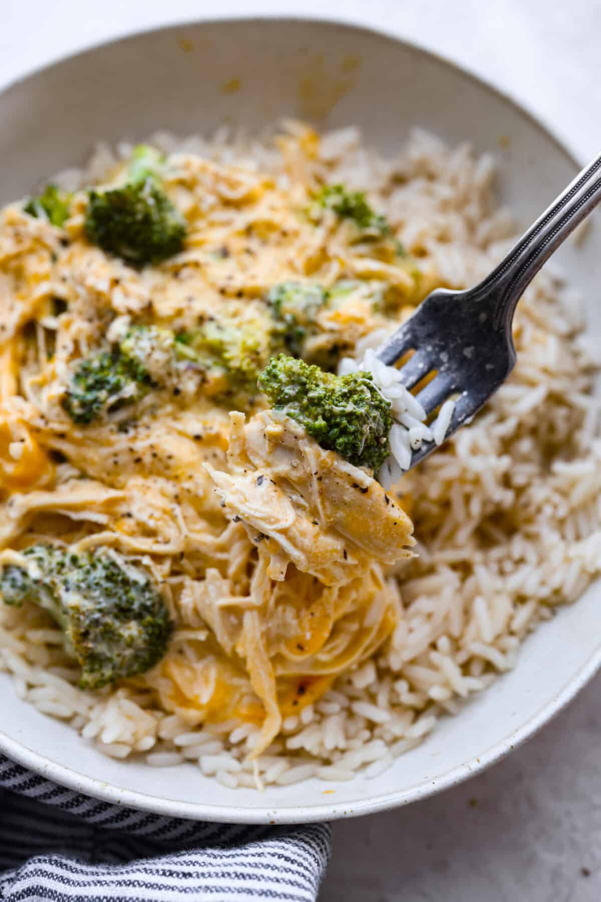 Close up shot of a bite of creamy chicken and rice over broccoli on a fork. 