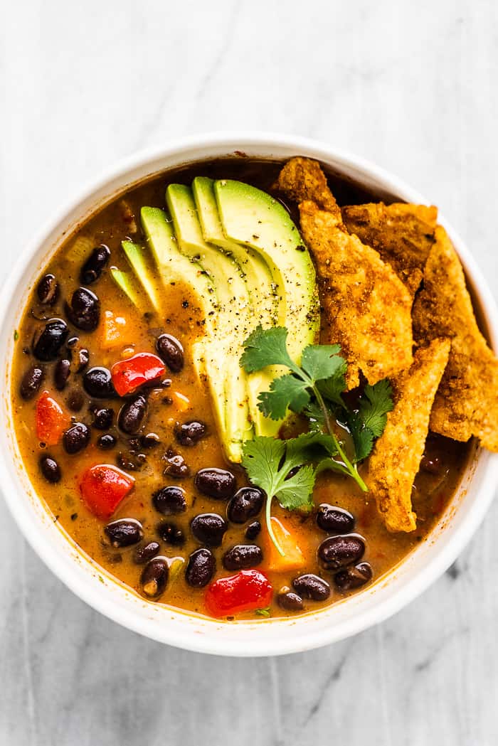 Black bean soup in a white bowl with avocado on top.