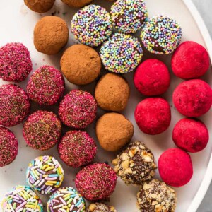 A white platter with multi-colored chocolate truffles.