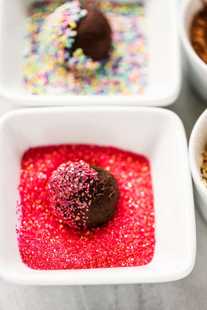 A chocolate truffle getting rolled in pink sugar.