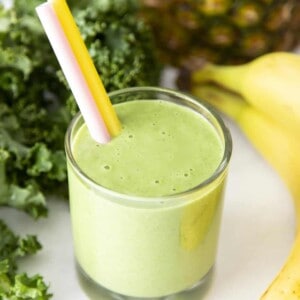 Kale smoothie in a glass surrounded by bananas, kale and pineapple