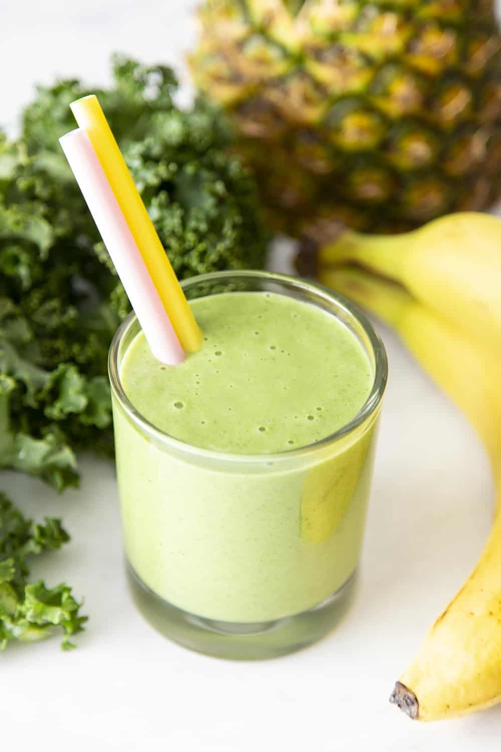 Kale smoothie in a glass surrounded by bananas, kale and pineapple