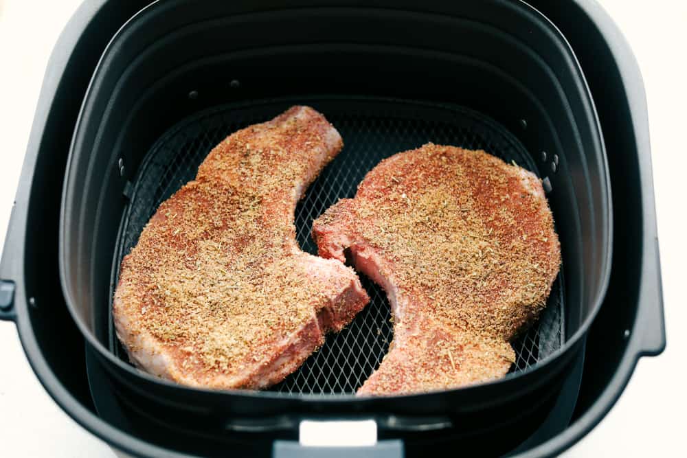 Seasoned pork chops in the air fryer basket. 