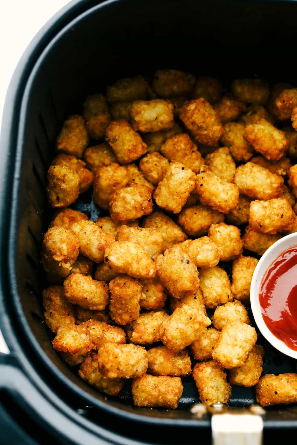 Golden and crispy tater tots in the air fryer with a side of ketchup. 