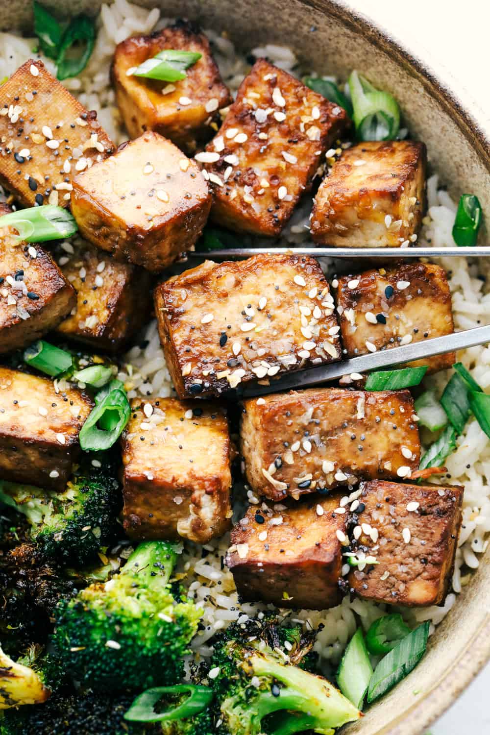 Using chopsticks to pick up air fried tofu with rice and broccoli. 