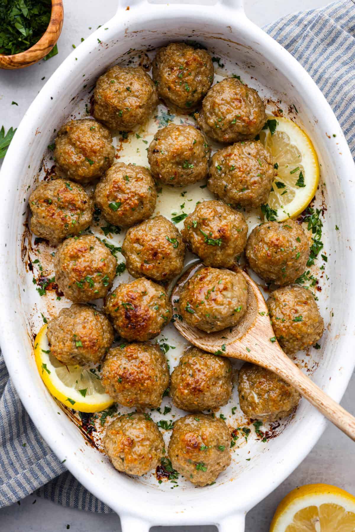 Top view of baked turkey meatballs in a white baking dish with a wooden spoon.