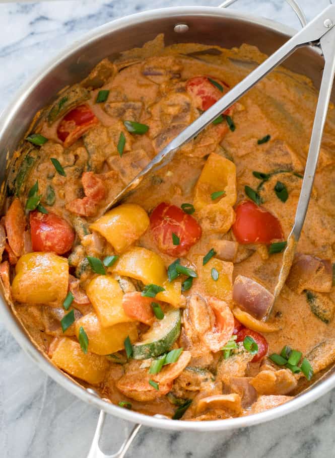 Vegetable curry in one pot with tongs stirring the pot. 