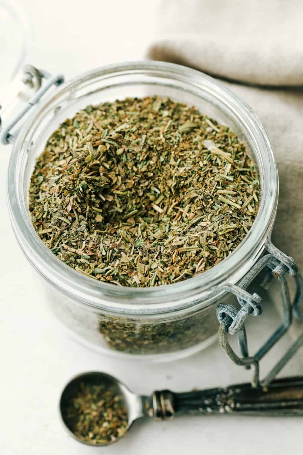 Italian seasoning in a glass jar with a teaspoon full beside it.