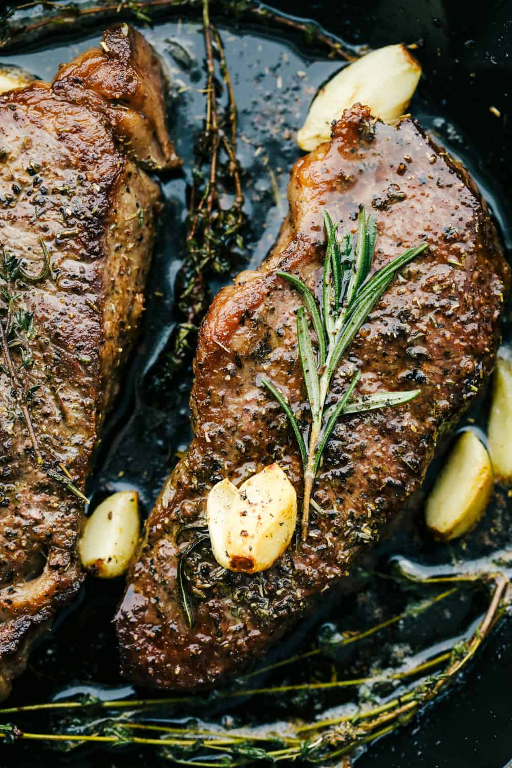 Two steaks in a black pan with garlic over top. 