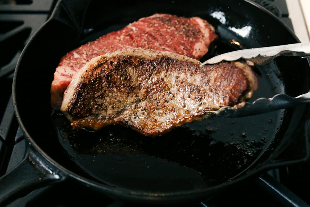 Steak in the pan being flipped. 