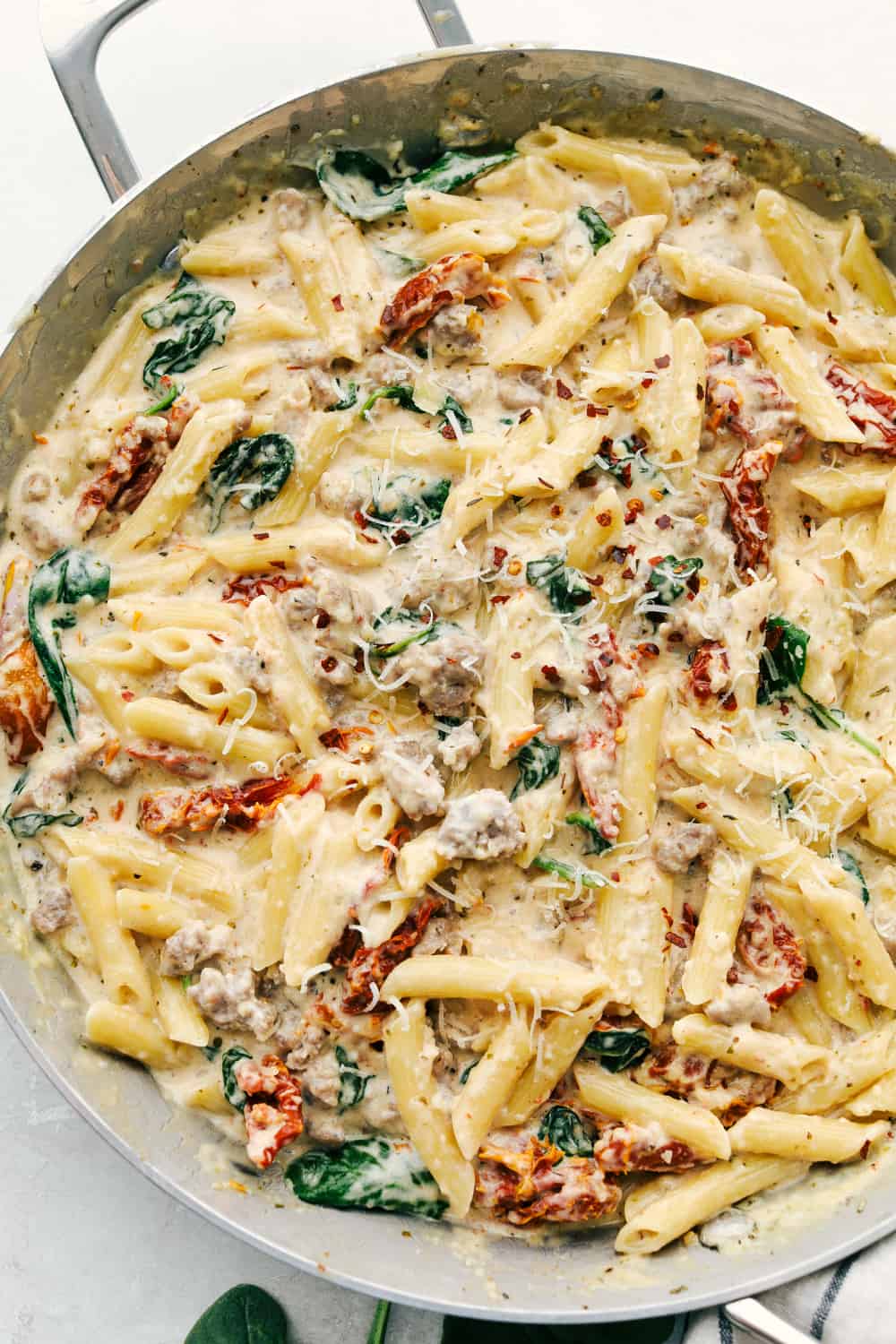 Creamy Tuscan Sausage Pasta in a pan garnished with parmesan cheese.