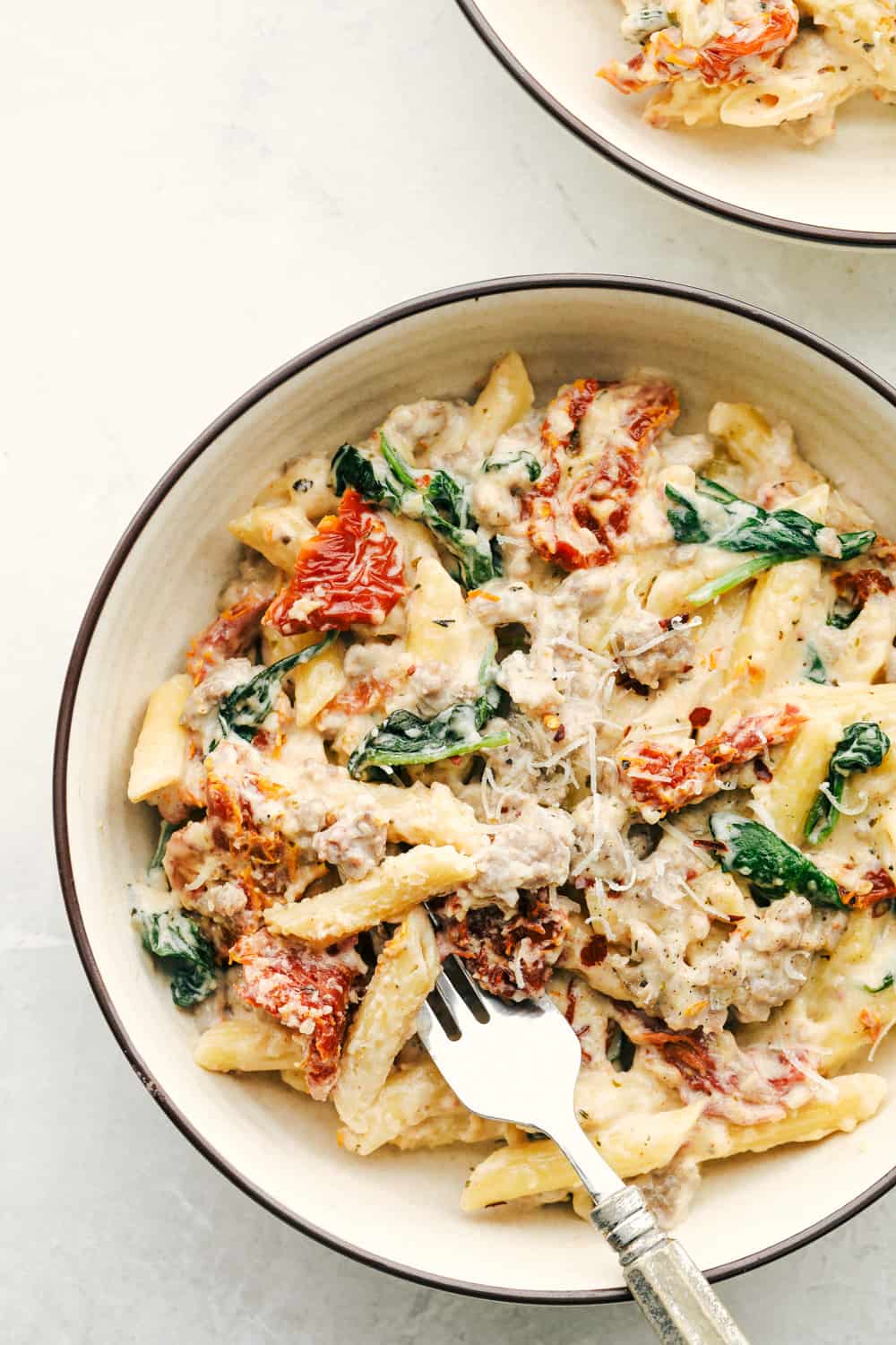 Tuscan sausage pasta in a white bowl with a fork. 