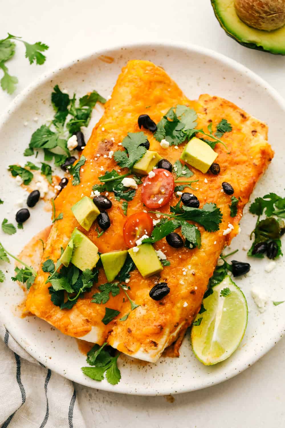 Two black bean and sweet potato enchiladas on a white plate with optional toppings.