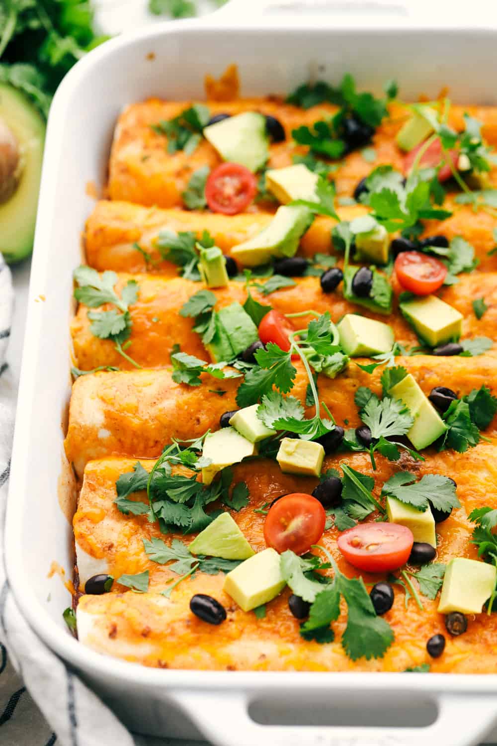 Sweet potato and black bean enchiladas cooked in a white dish with avocado and tomatoes.