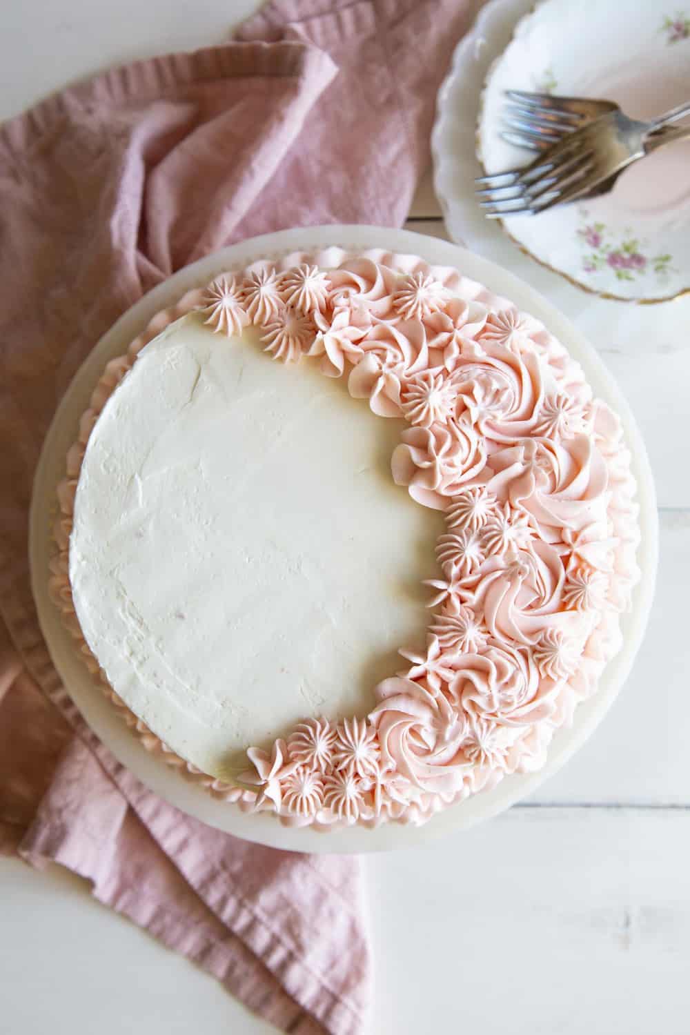 Pink velvet cake with white frosting and pink flowers.