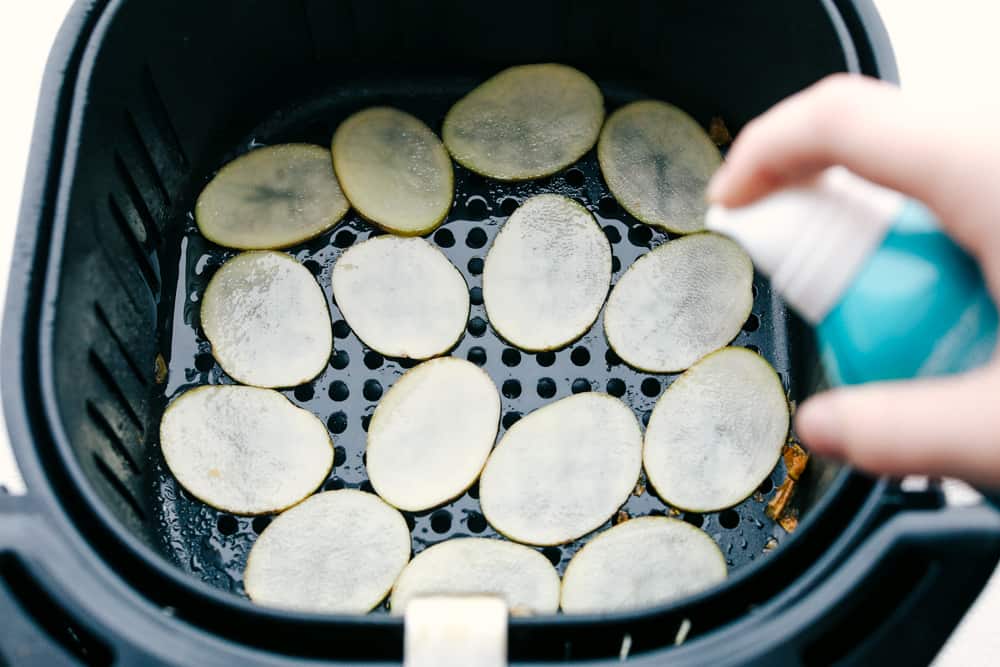 Spritzing sliced potatoes in air fryer with oil. 