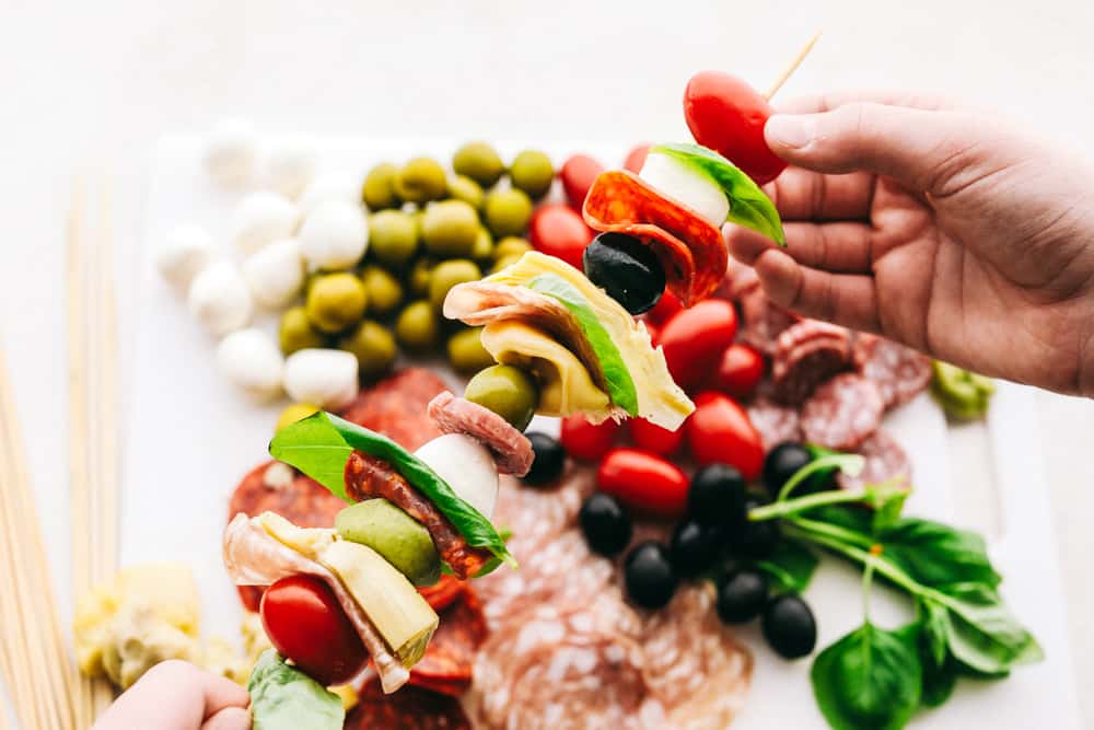 Layering ingredients on skewers for antipasto skewers. 