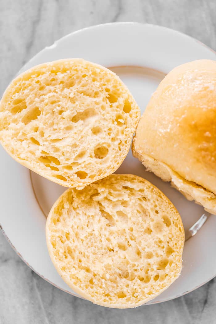 A potato bun on a plate cut in half.