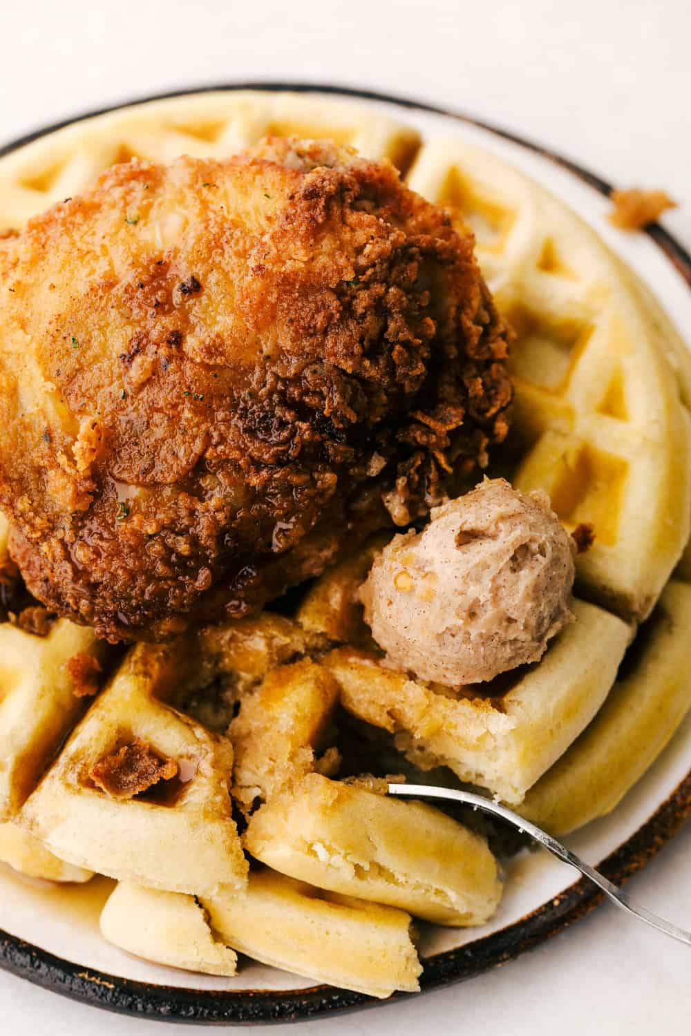 Chicken and waffles on a plate with cinnamon butter, syrup with a bite on a fork. 