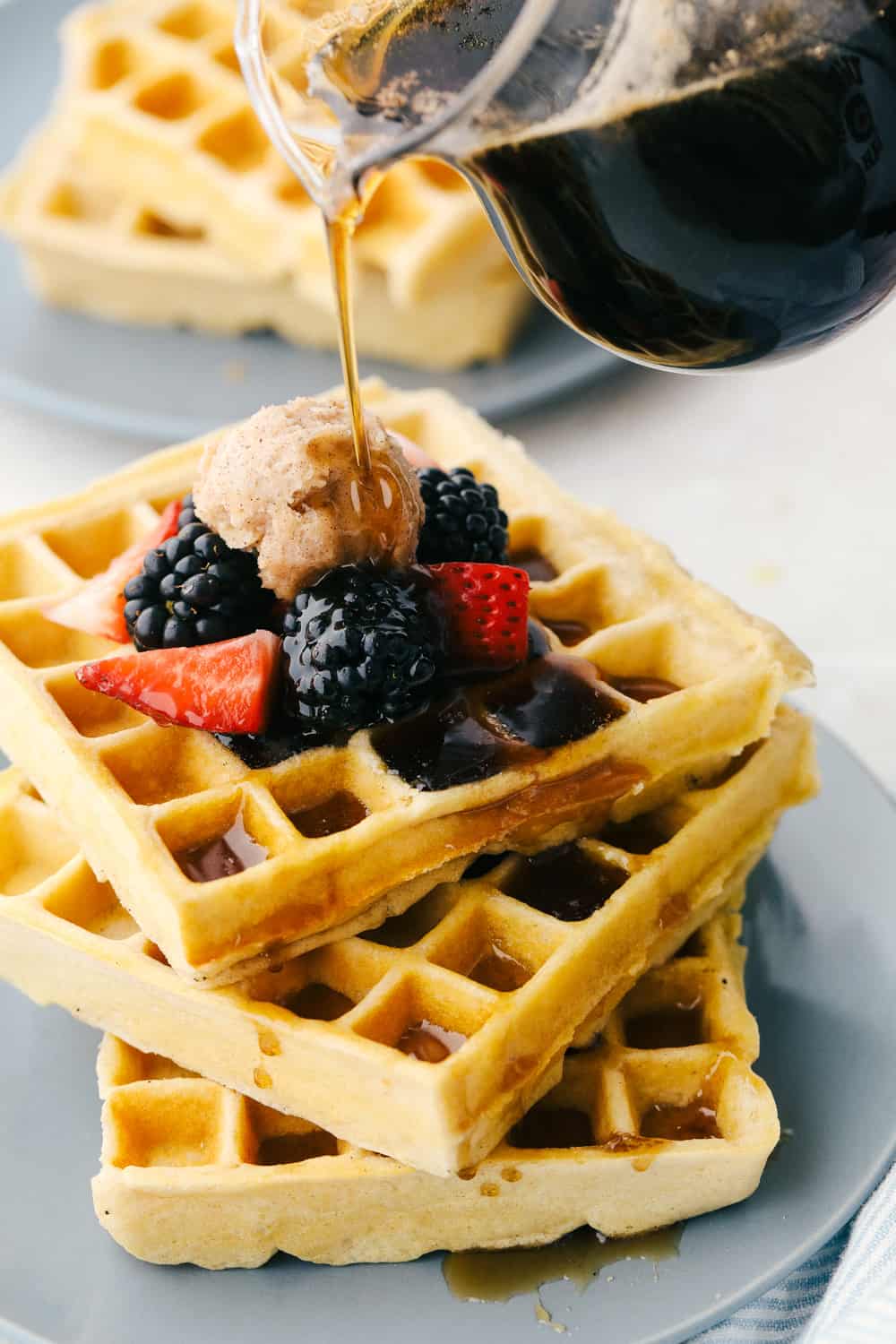 Drizzling syrup on top of a stack of homemade waffles. 