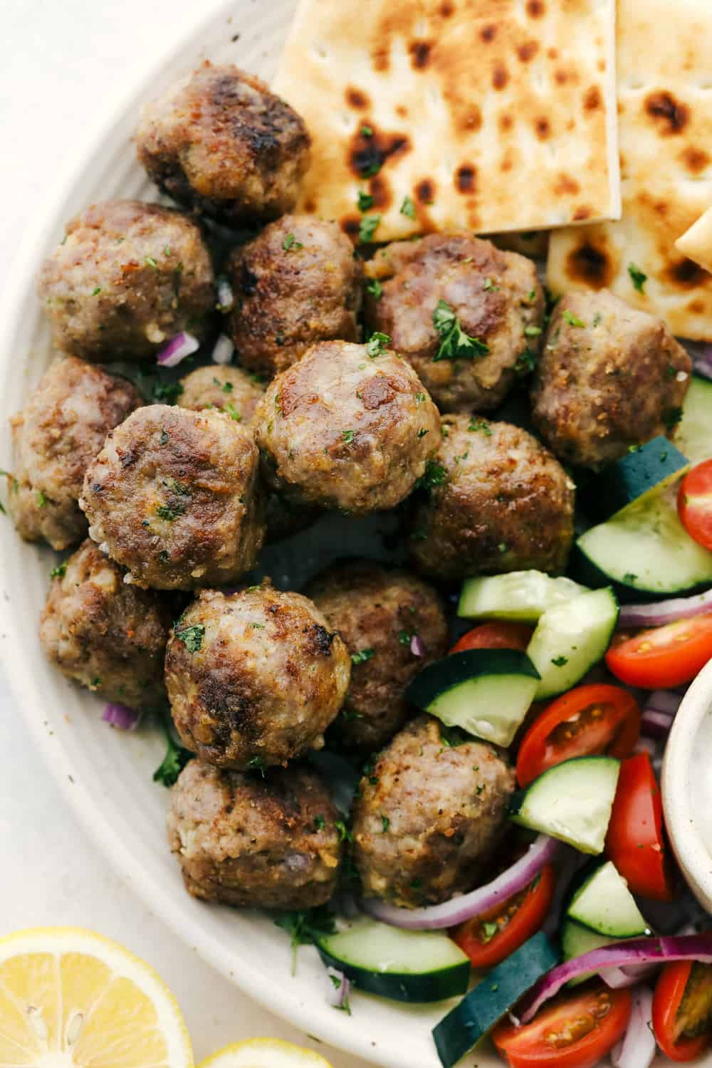 Browned meatballs on a platter with pitas and vegetables.