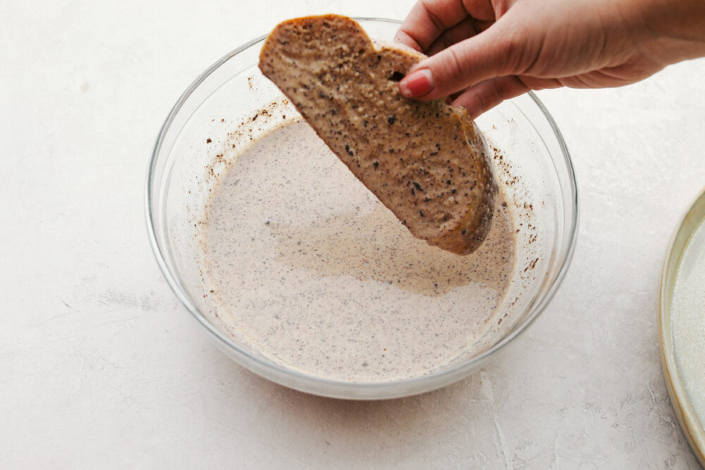 Challah bread being dipped in a bowl of egg mixture. 