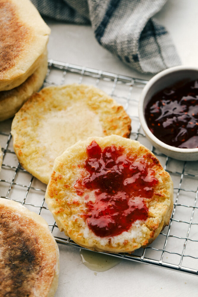 Toasted english muffins on a cooling rack with butter and jam. 